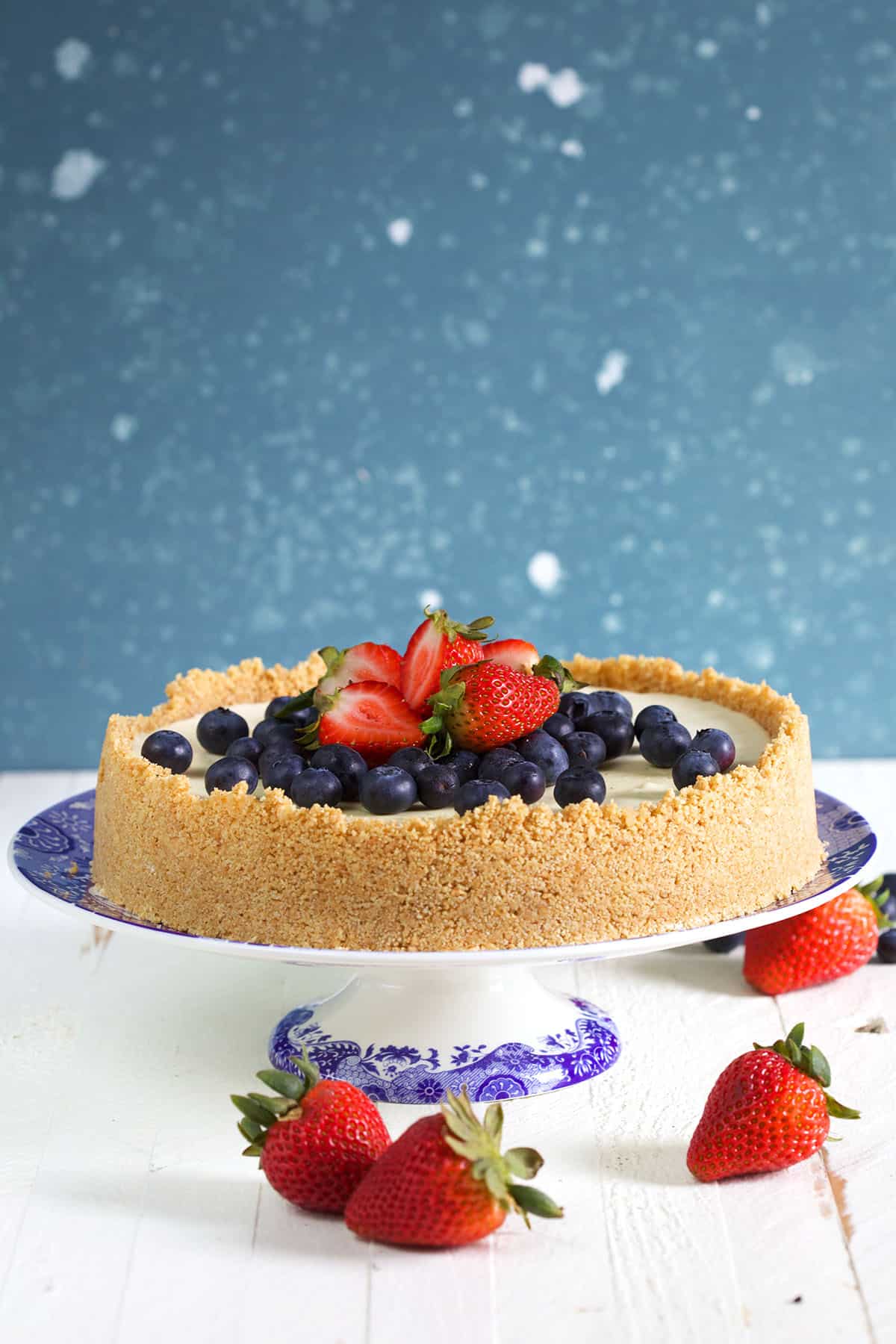 No Bake Cheesecake with graham cracker crust on a cake plate with berries on top