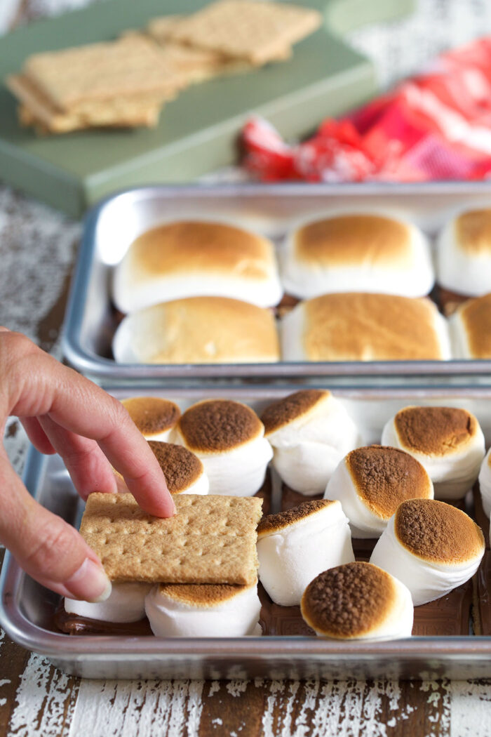 A graham cracker is being placed on top of a baked s'more. 