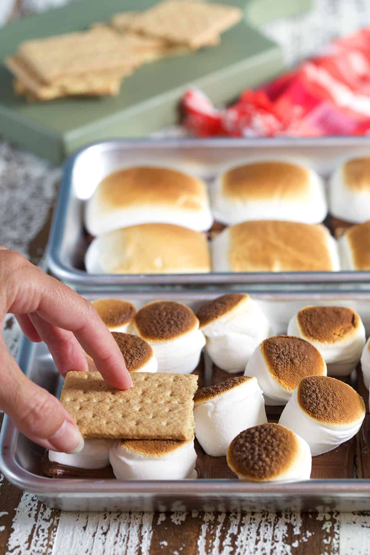 A graham cracker is being placed on top of a baked s'more. 