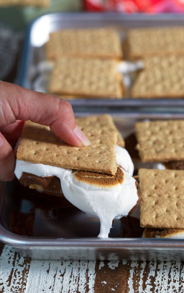 A hand is lifting a s'more from the baking dish. 