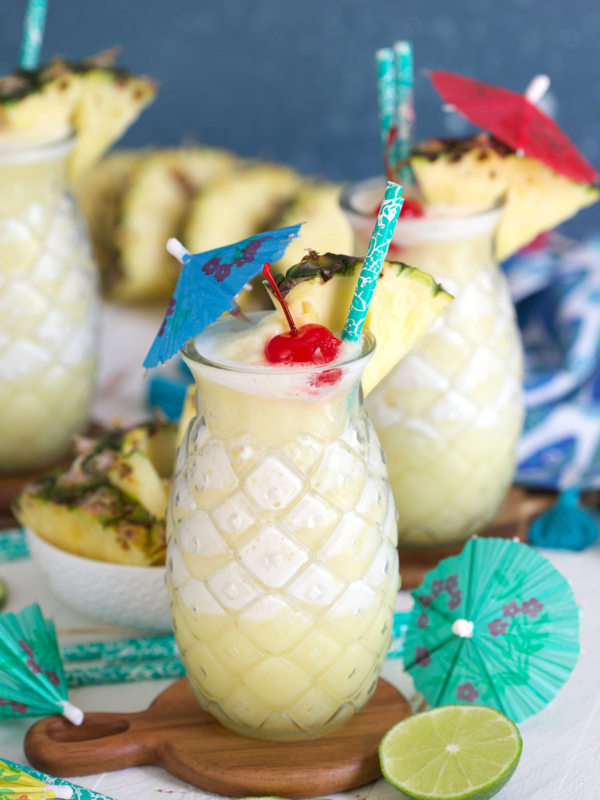 Several pina coladas are placed on wooden coasters on a white surface.