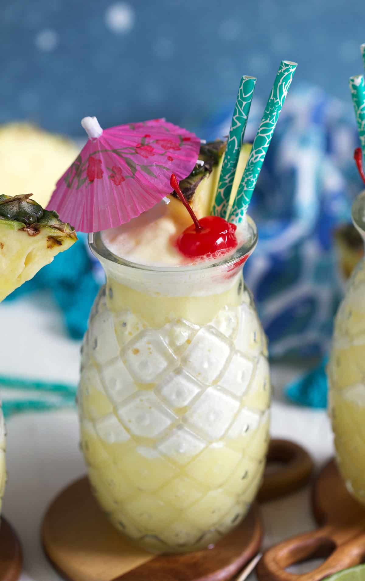 A glass of pina colada cocktail is garnished with an umbrella, pineapple and cherry. 