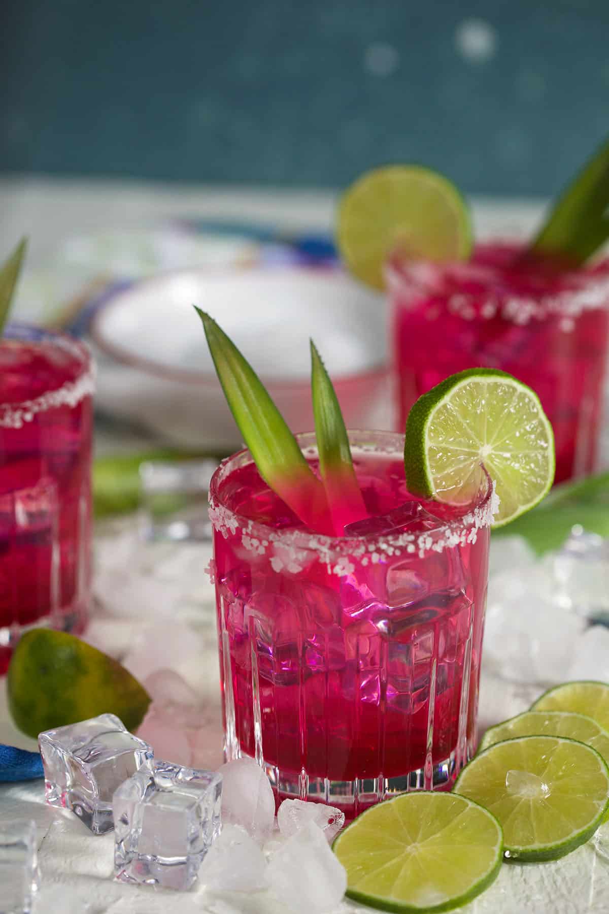Ice cubes and lime slices are placed around a glass of pink margarita. 