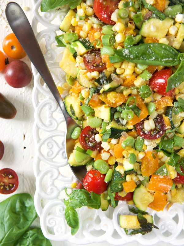 A large serving spoon is placed on a platter full of succotash.
