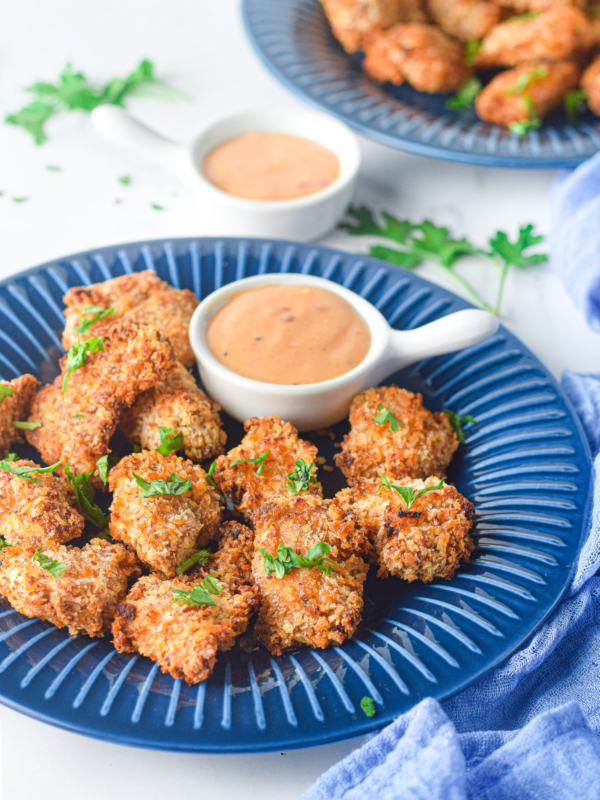 A blue plate is filled with cooked bang bang chicken and a small white bowl of dipping sauce.