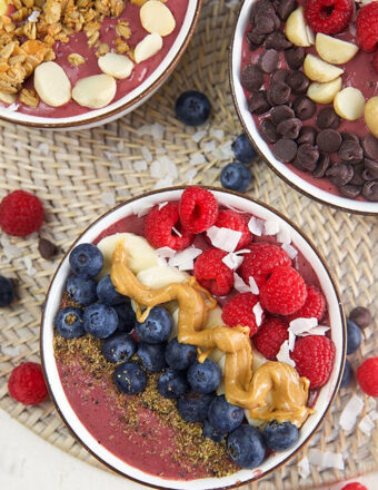 three Acai bowls with a variety of toppings on a wicker placemat