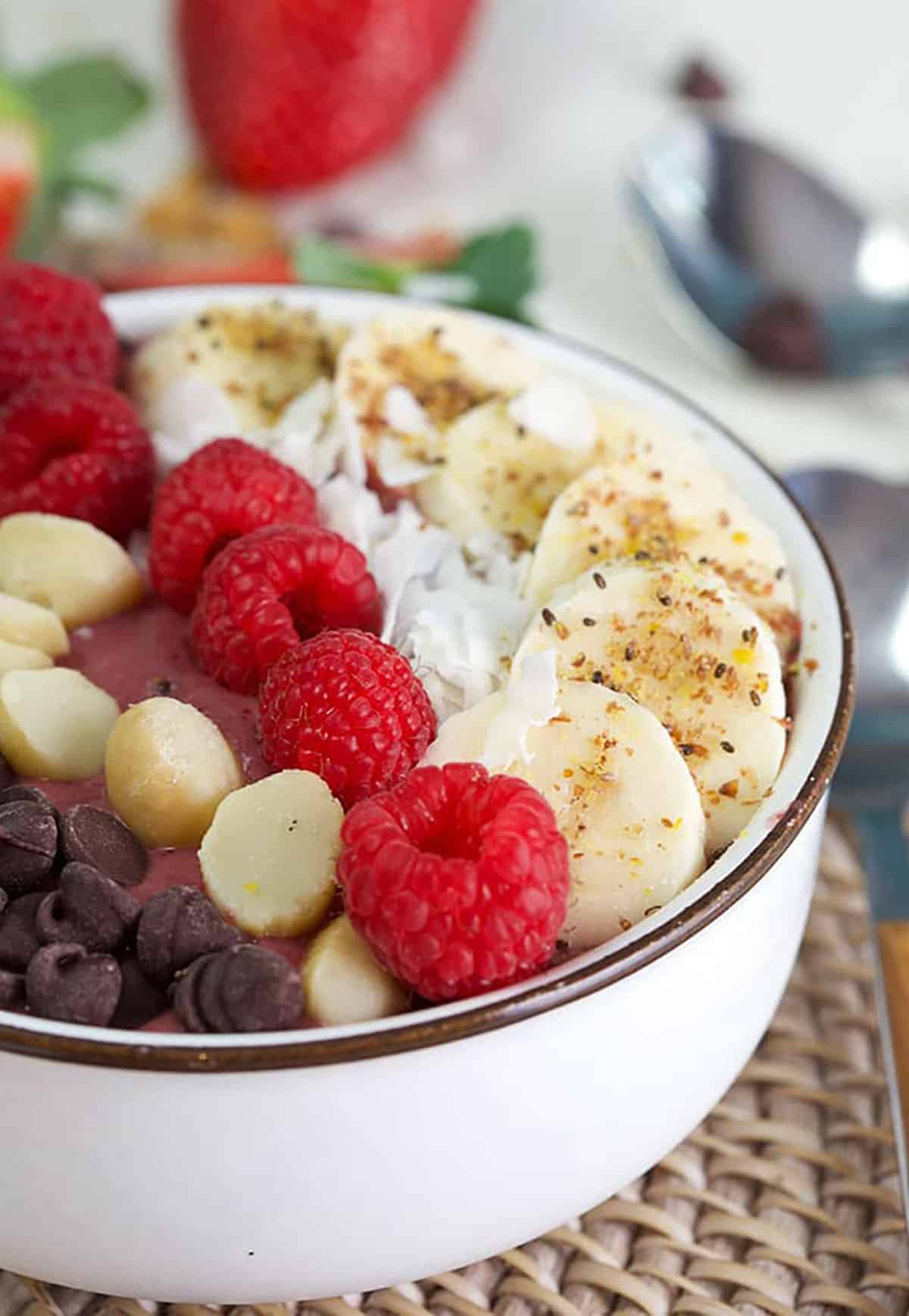 close up of Acai bowl topped with bananas, hemp seed, raspberry and nuts