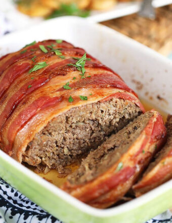 Bacon wrapped meatloaf in a green and white baking dish.