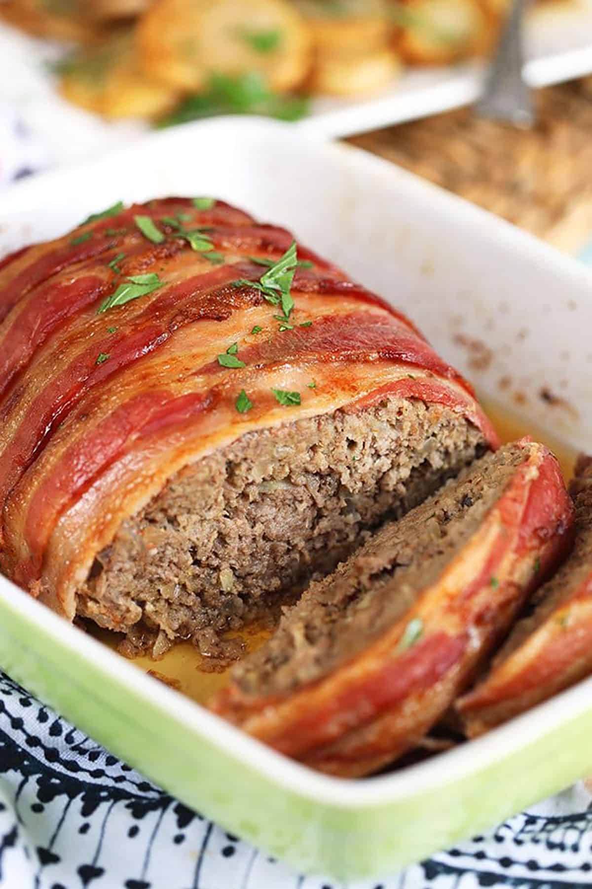 Bacon wrapped meatloaf in a green and white baking dish.