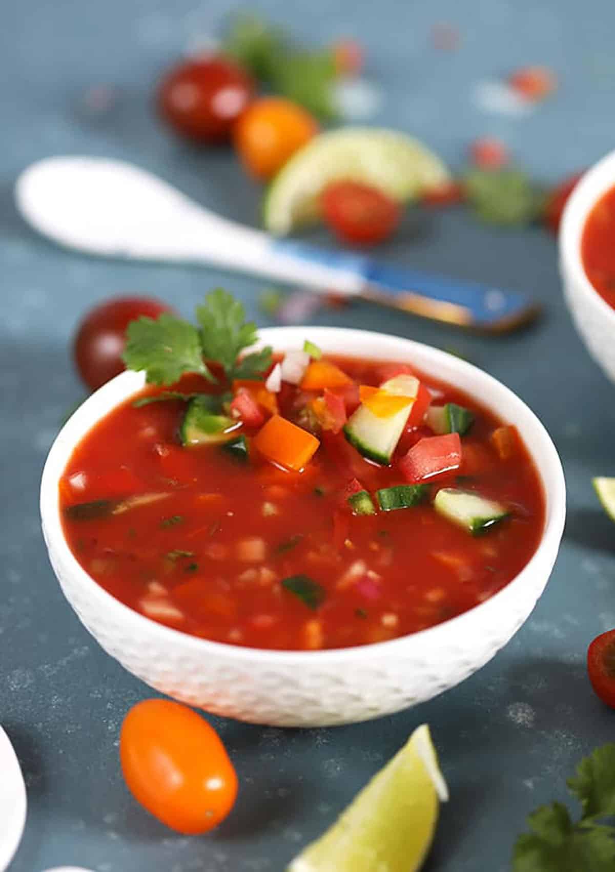 Tomato Gazpacho in a white bowl with limes and a white spoon 