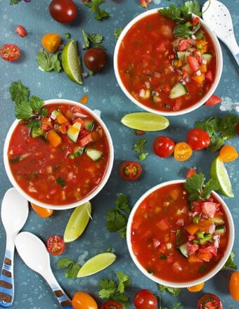 three white bowls with gazpacho on a blue background.