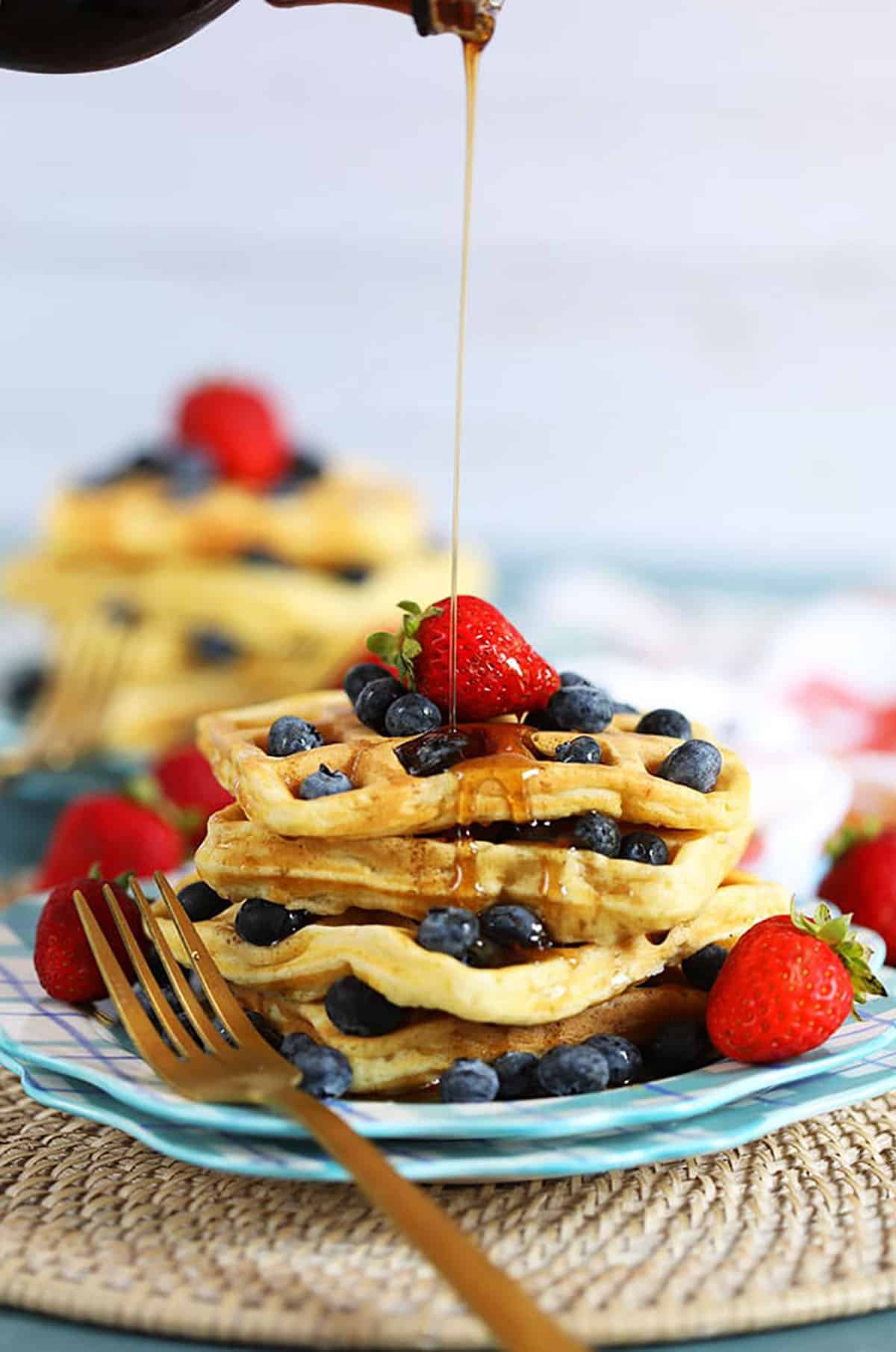 Stack of waffles with berries and syrup being drizzled from thesuburbansoapbox.com