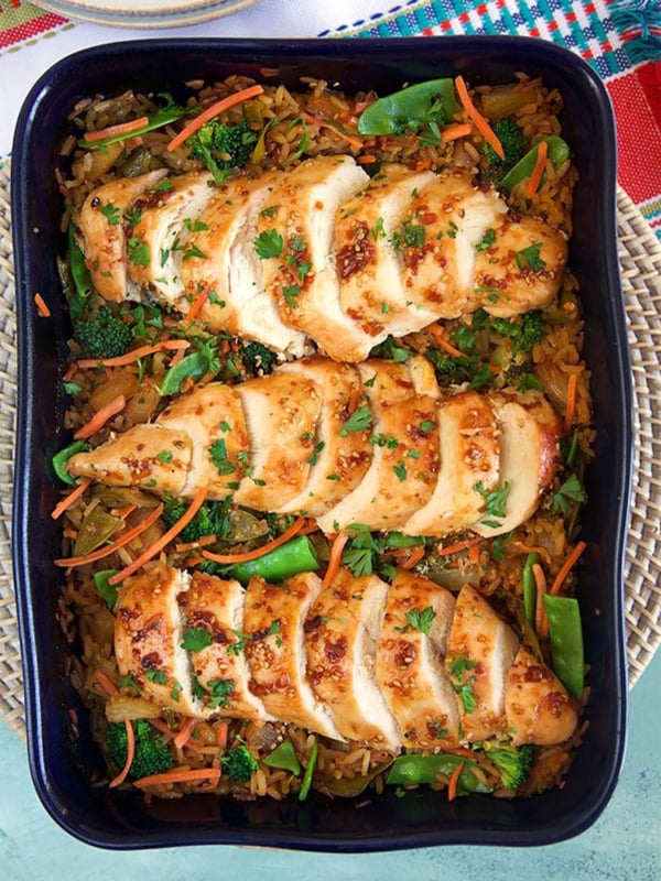 Overhead shot of Baked Teriyaki Chicken Casserole on a bed of rice with veggies in a blue casserole dish.