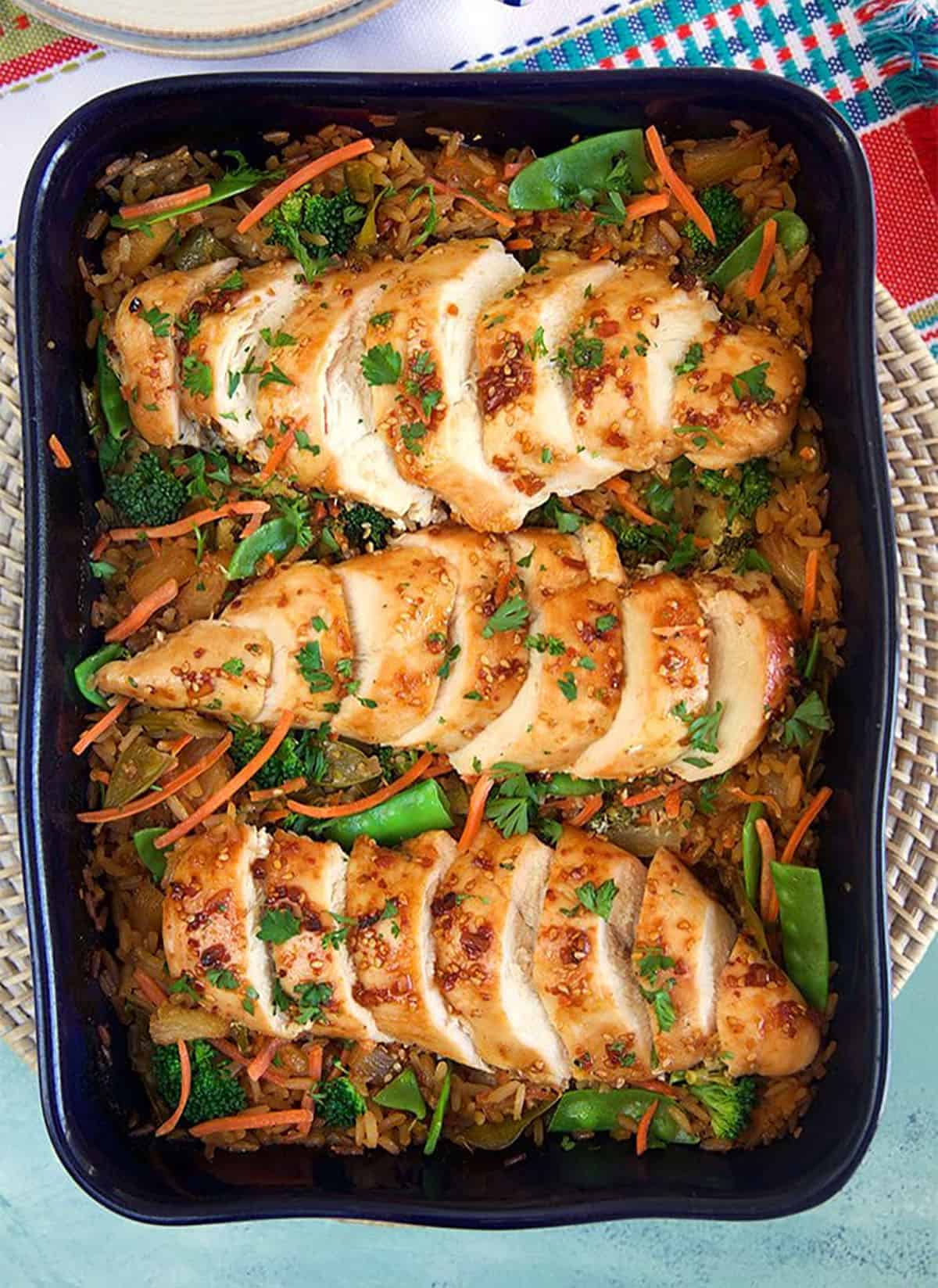 Overhead shot of Baked Teriyaki Chicken Casserole on a bed of rice with veggies in a blue casserole dish.