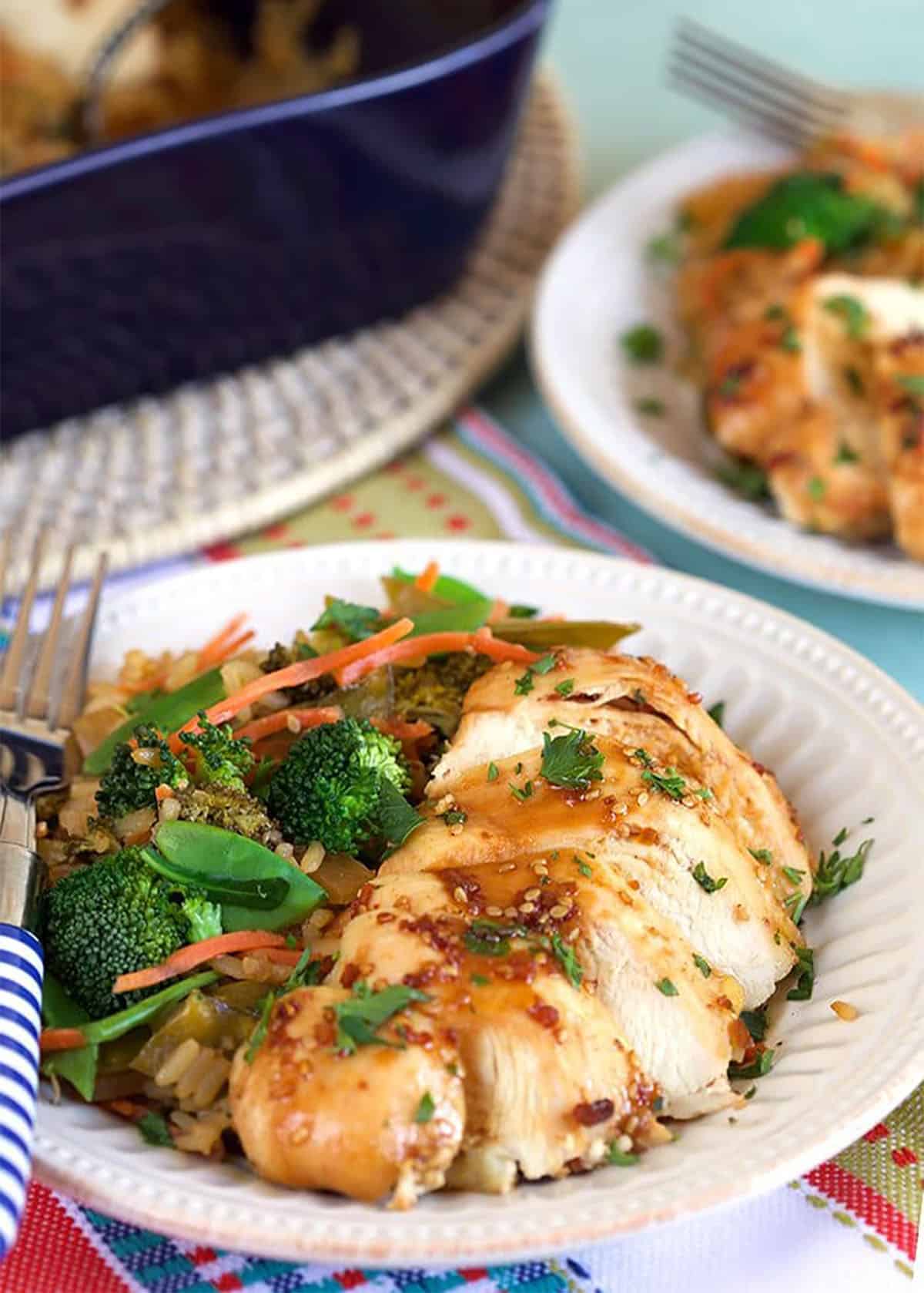 Close up of sliced baked teriyaki chicken breast on a white plate with rice and veggies.