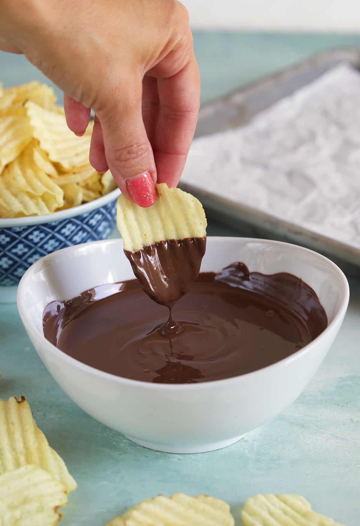 A potato chip is being dipped into warm chocolate. 