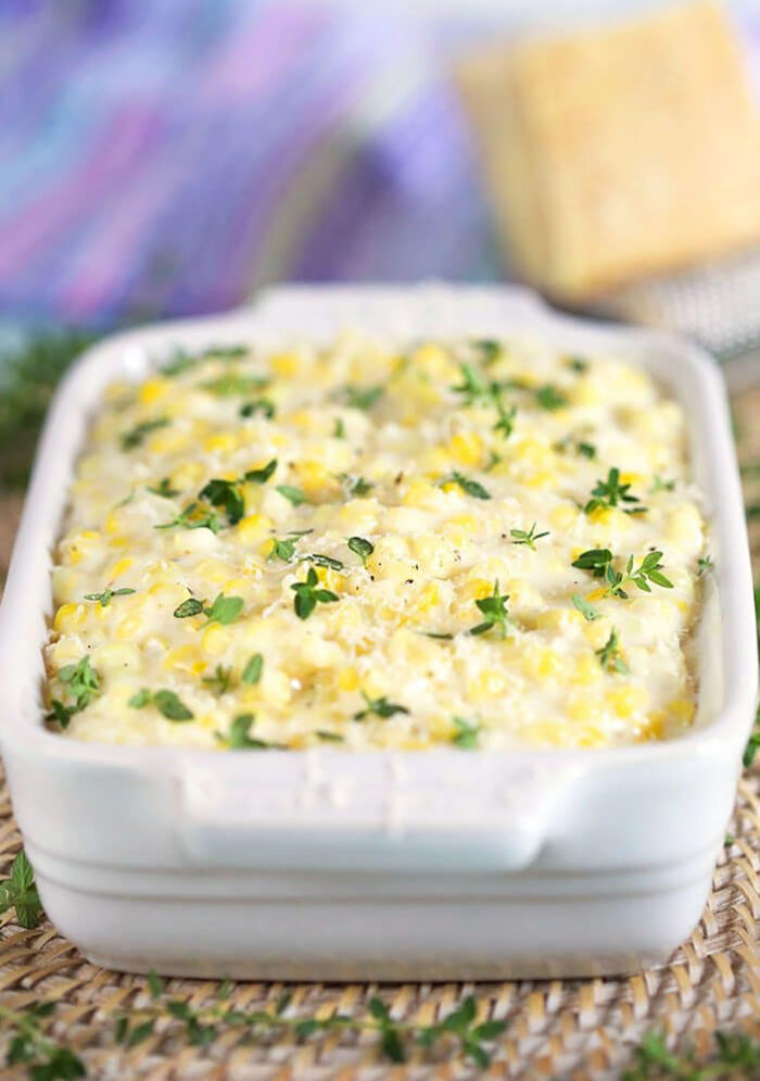 Creamed Corn in a white dish with a wedge of cheese in the back.