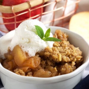 Crock Pot apple crisp in a white ramekin with whipped cream on top