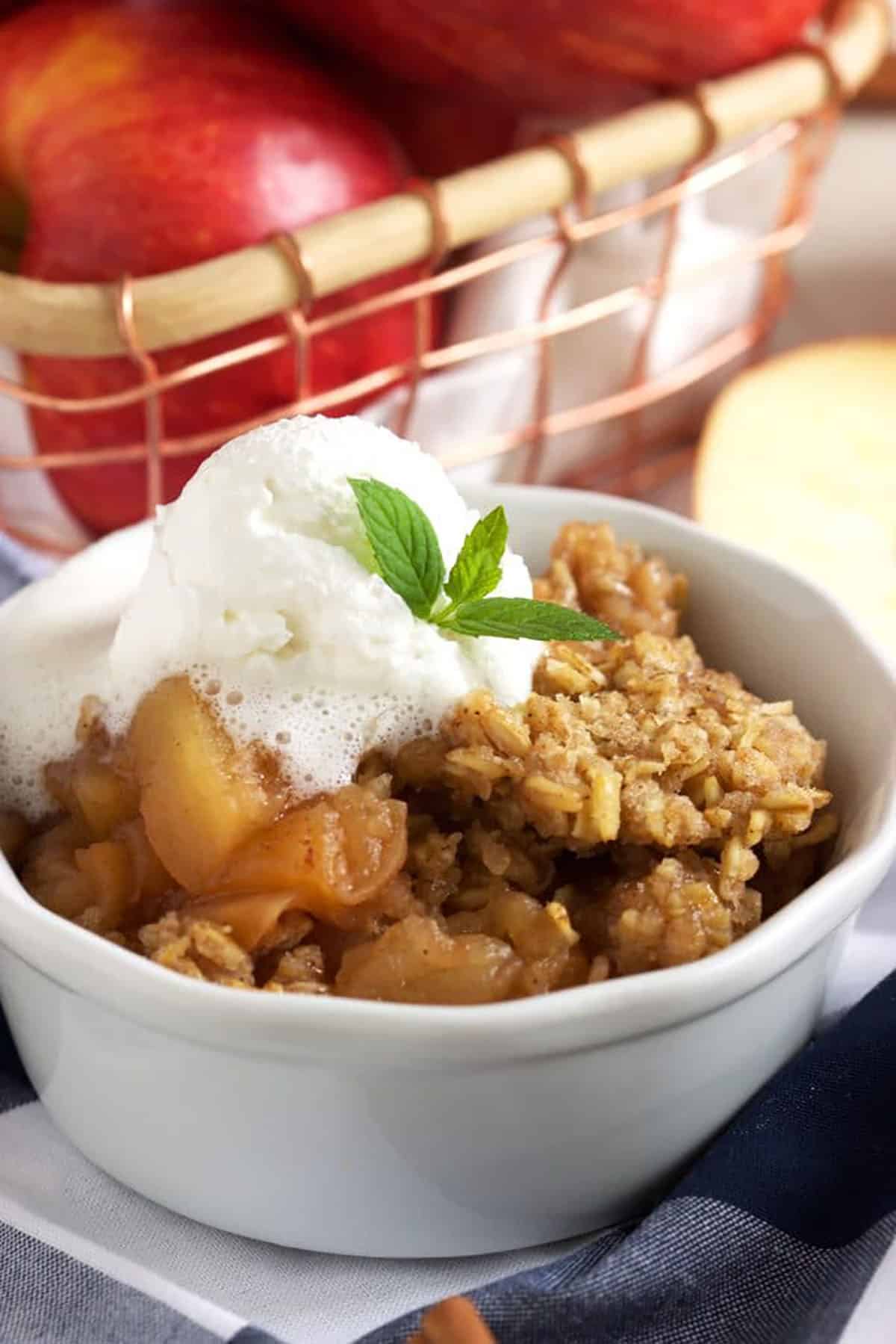 Crock Pot apple crisp in a white ramekin with whipped cream on top