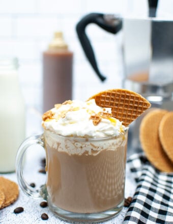 A latte is topped with whipped cream and a piece of waffle cone on a white surface.