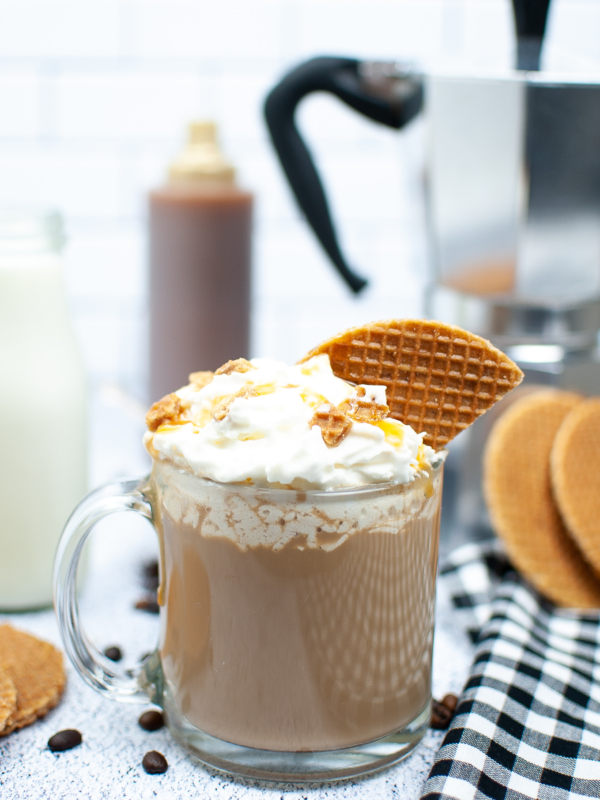 A latte is topped with whipped cream and a piece of waffle cone on a white surface.