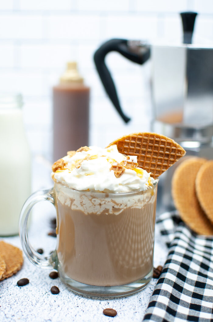 A latte is topped with whipped cream and a piece of waffle cone on a white surface. 