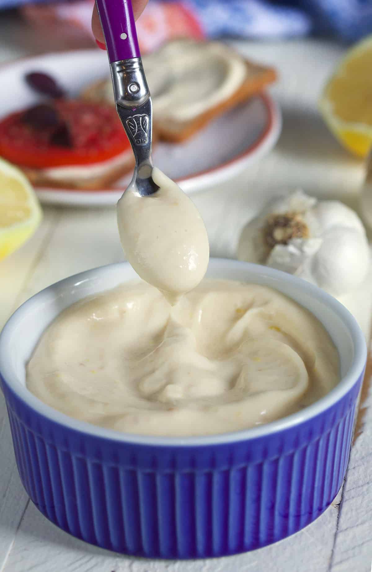 Garlic Aioli in a blue bowl with a scoop on a purple spoon.