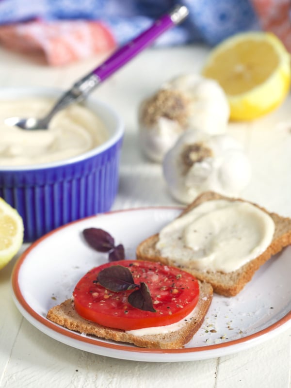 Tomato on a small slice of bread with aioli spread on a second slice on a white plate.