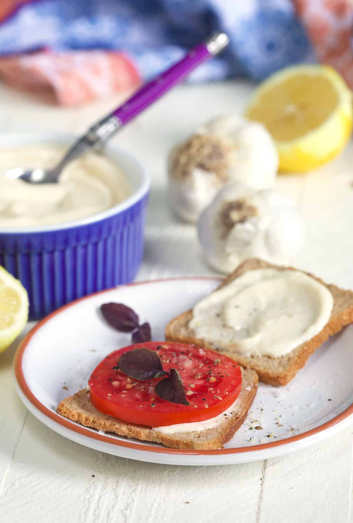 Tomato on a small slice of bread with aioli spread on a second slice on a white plate.