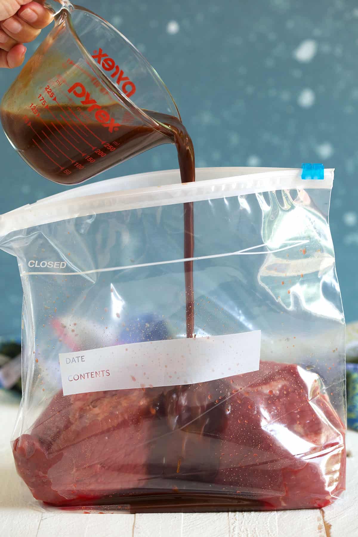 Marinade is being poured into a bag with a cut of red meat in it. 