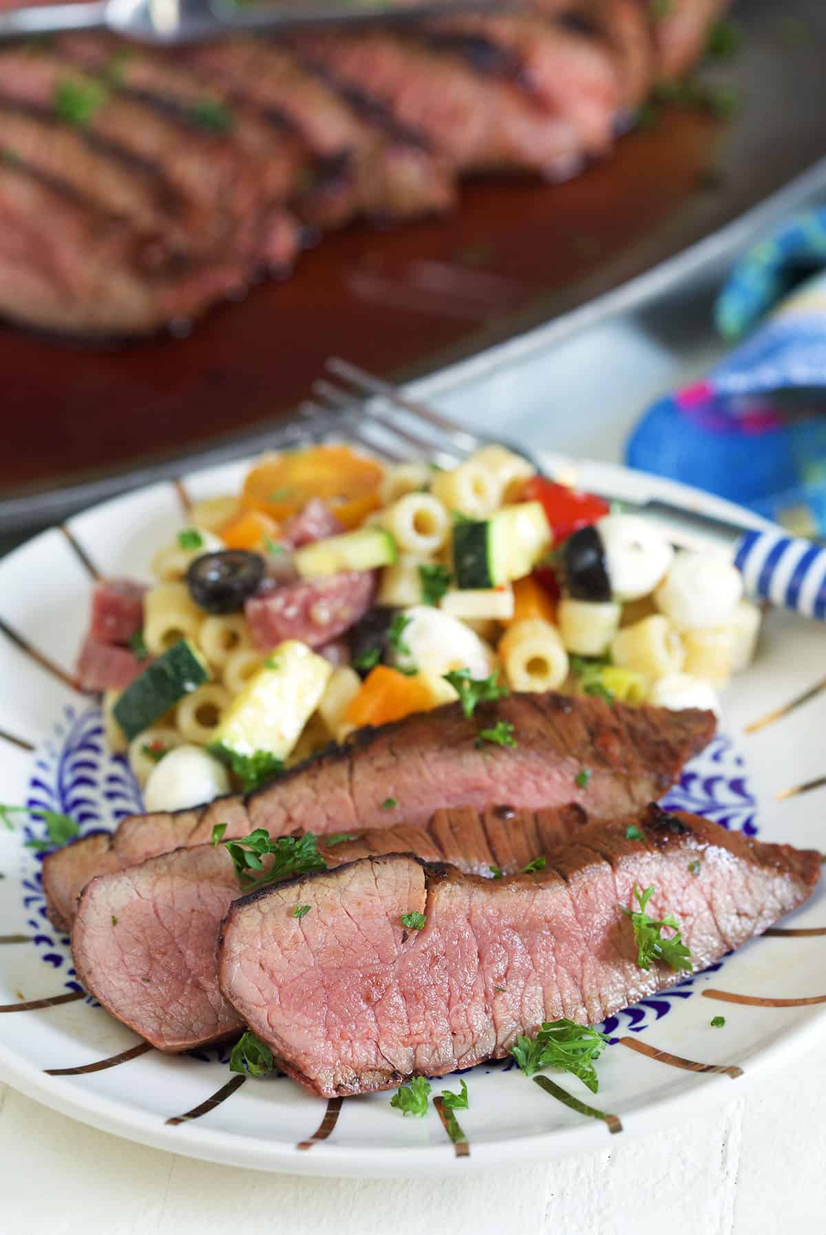Several pieces of steak are plated with pasta salad. 
