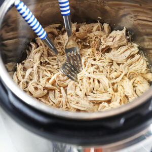 Shredded chicken in an Instant Pot with two forks.