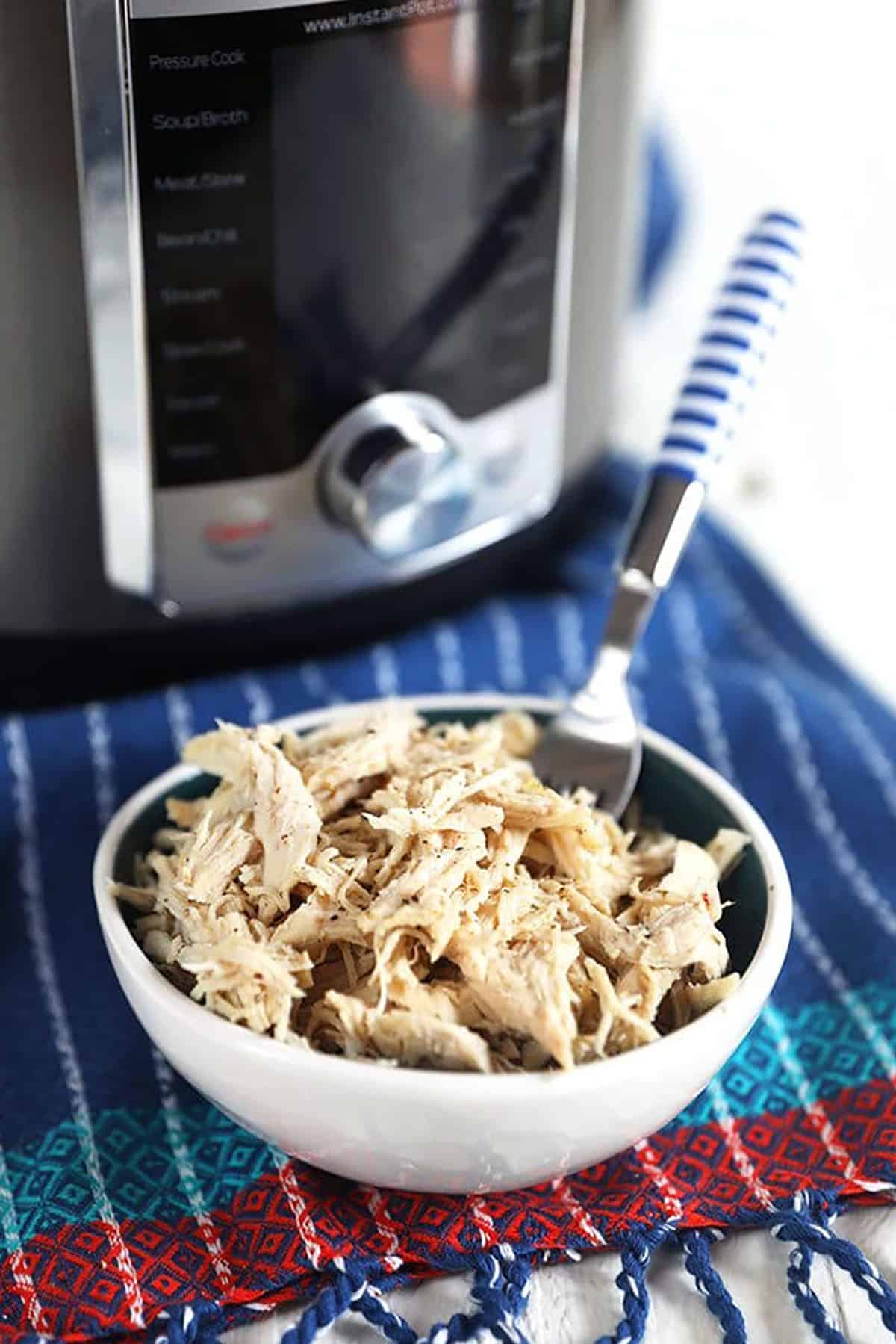 Shredded chicken breast in a white bowl with a blue and white fork.