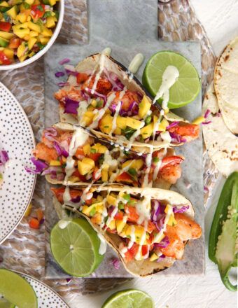 Three lobster tacos are placed on a table next to halved limes.
