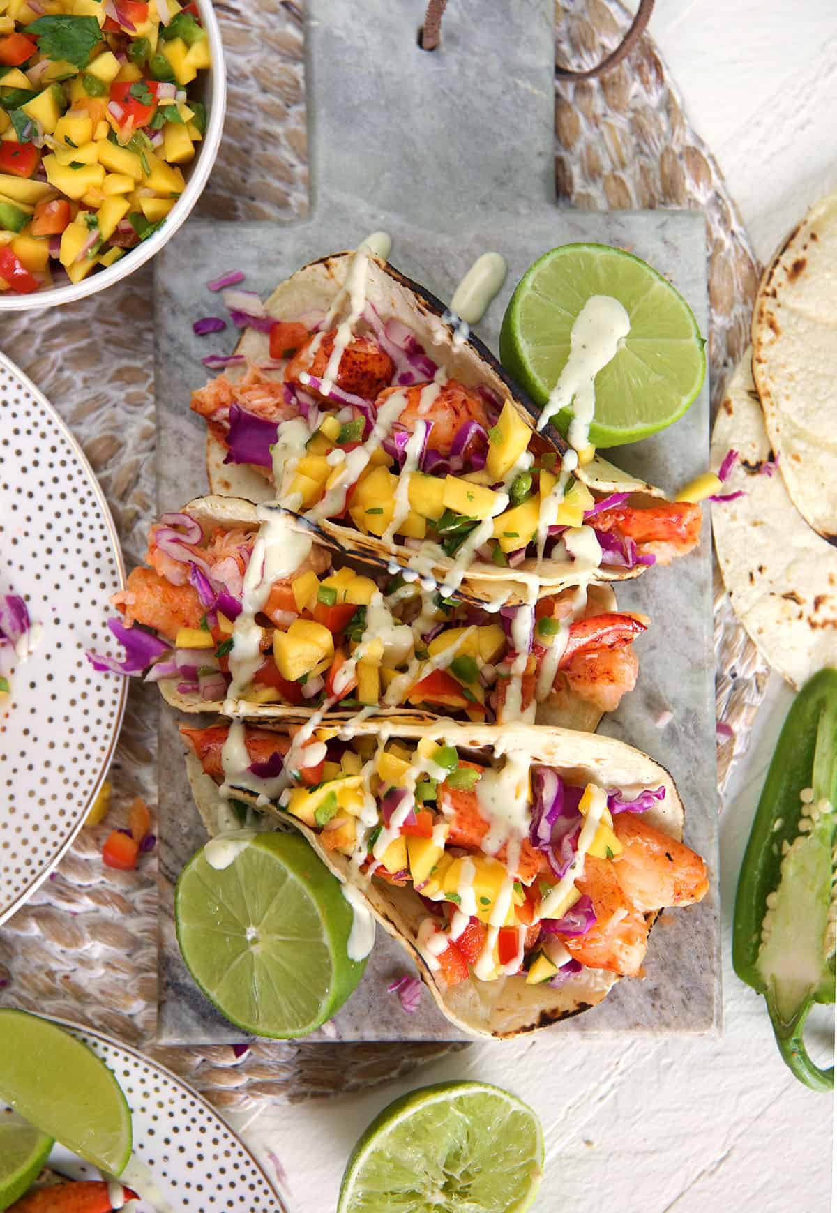 Three lobster tacos are placed on a table next to halved limes. 