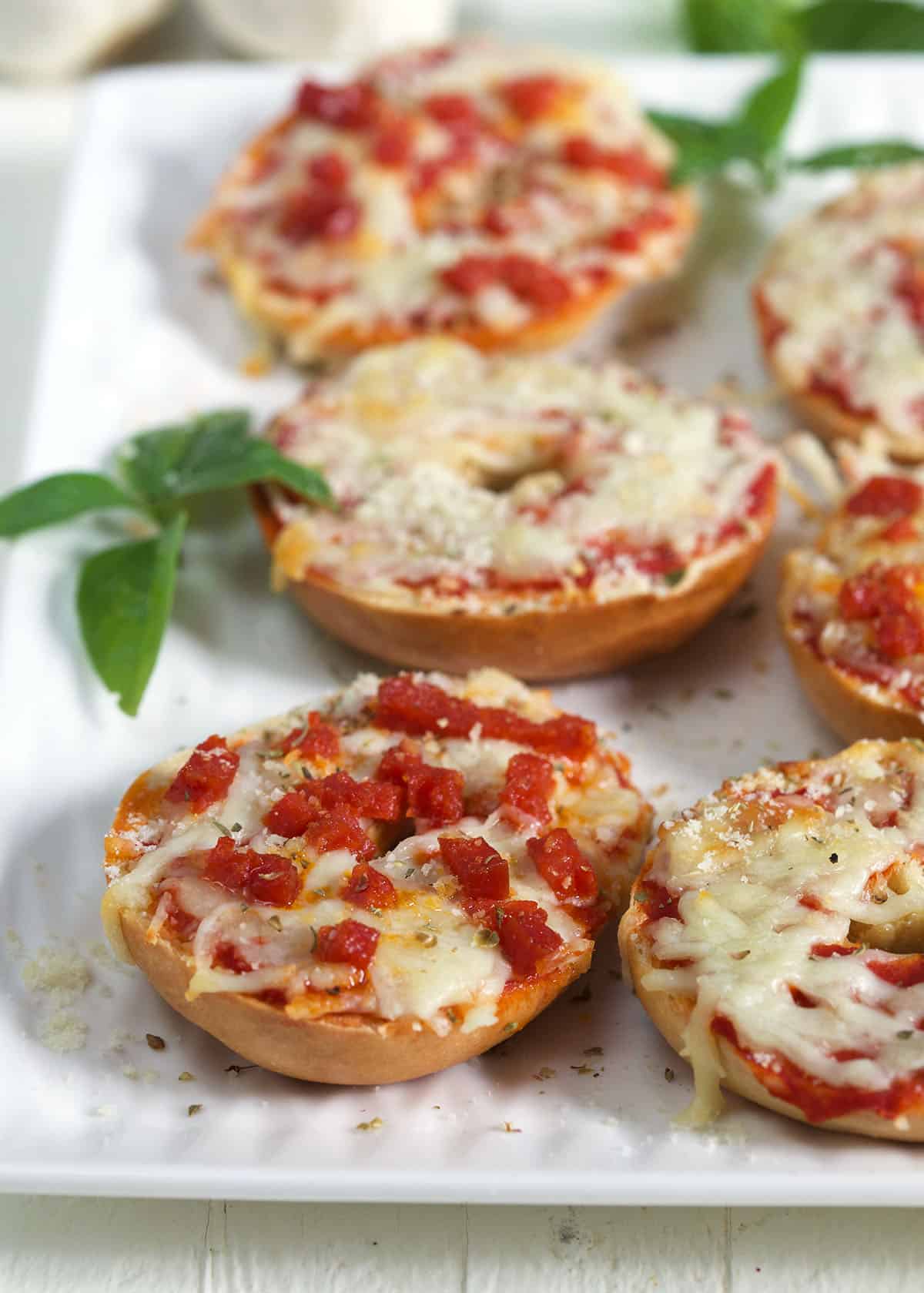 A bagel topped with pepperoni pieces is placed on a white serving tray. 