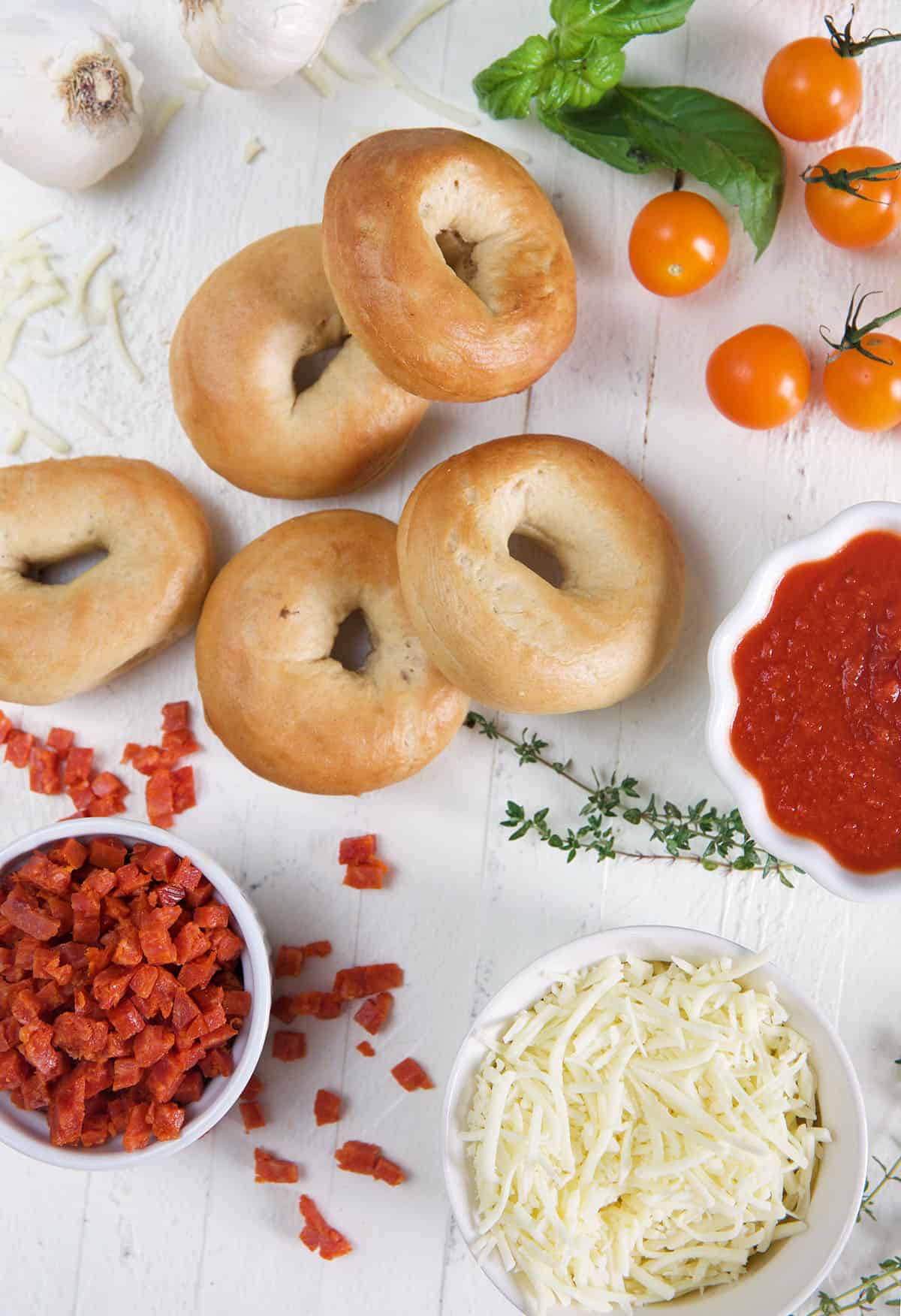 The ingredients for mini pizza bagels are placed on a white surface. 