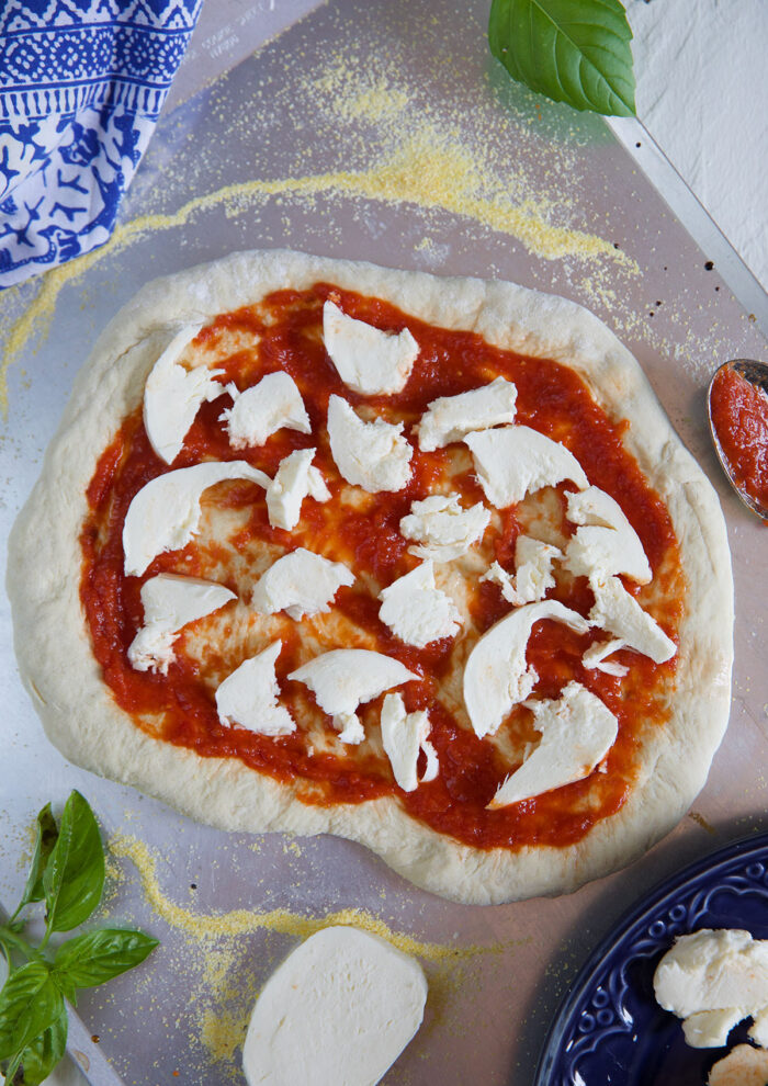 Pieces of mozzarella cheese are placed on a pizza dough circle with tomatoes. 