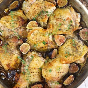 Crispy chicken thighs with roasted figs in a steel skillet on a white background.
