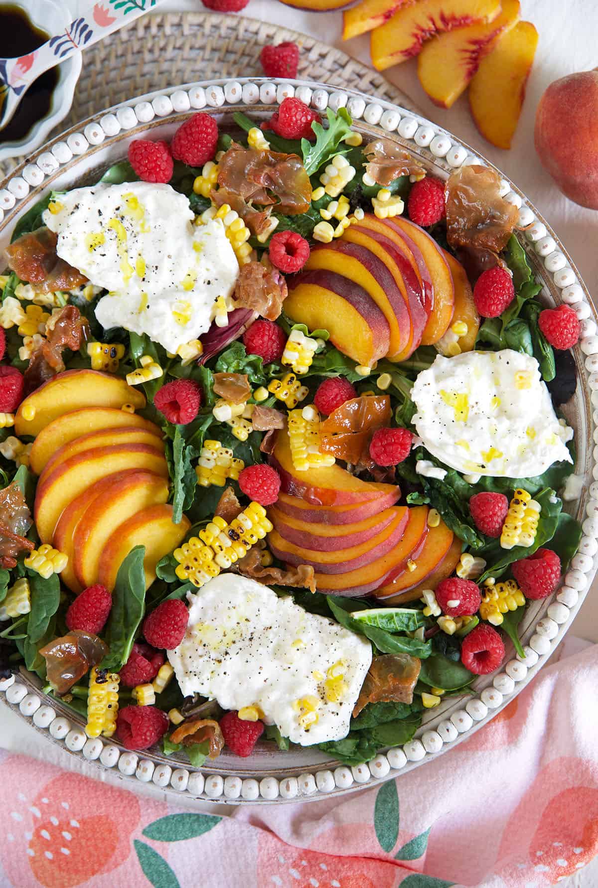 A large white serving bowl is filled to the brim with peach burrata salad. 