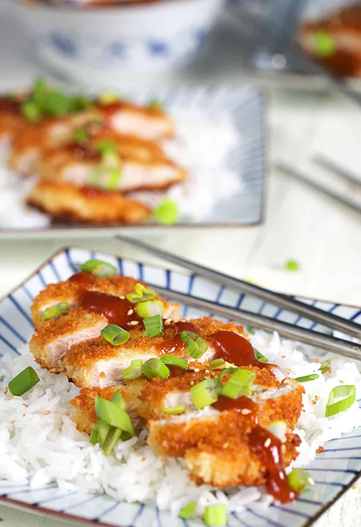 Pork Katsu on rice plated on a square plate sprinkled with chopped green onions.