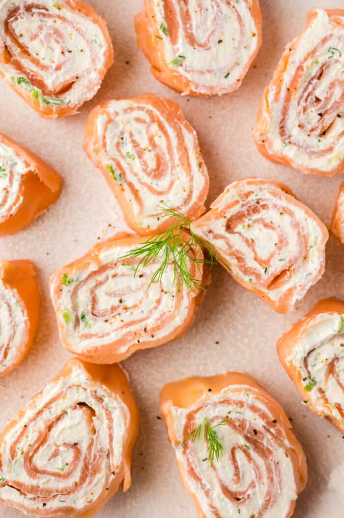 Several smoked salmon pinwheels are placed on a tan surface. 