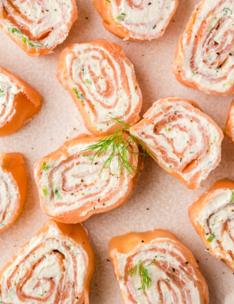 Several smoked salmon pinwheels are placed on a tan surface.