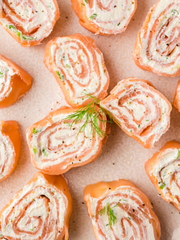 Several smoked salmon pinwheels are placed on a tan surface.