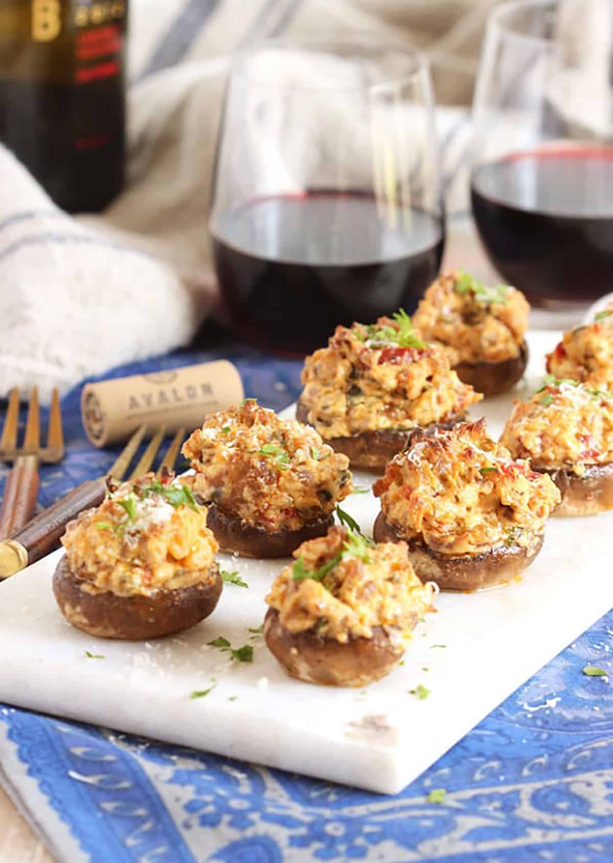 Sausage stuffed mushrooms on a marble platter with a bottle of wine in the background.