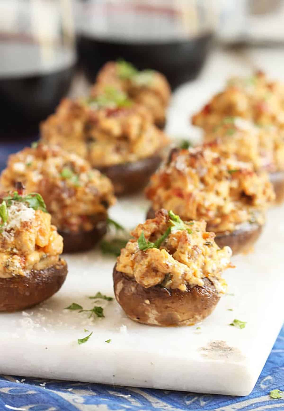 Eight Sausage Stuffed Mushrooms on a marble board with two glasses of wine in the background.