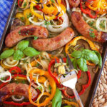 Sheet Pan Sausage and peppers with basil and onions with a serving fork.