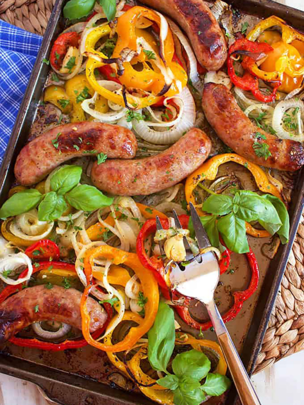 Sheet Pan Sausage and peppers with basil and onions with a serving fork.
