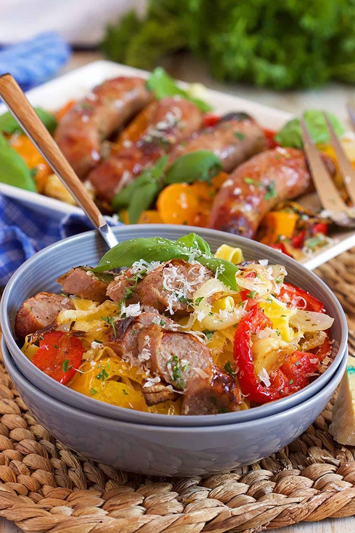 Sheet Pan Sausage and Peppers on pasta in a blue bowl with a wooden fork.