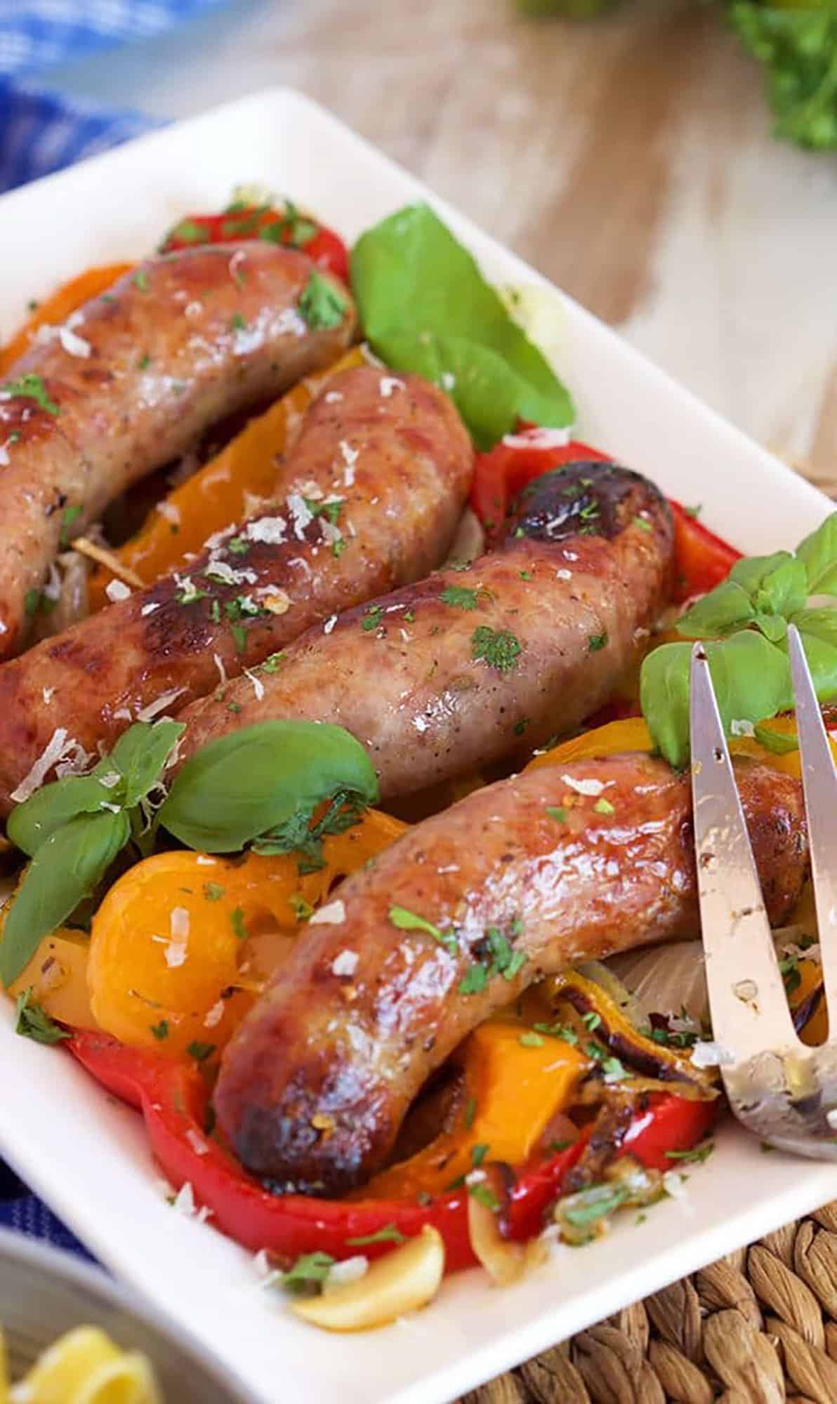 Italian sausage with peppers on a white platter garnished with basil leaves.